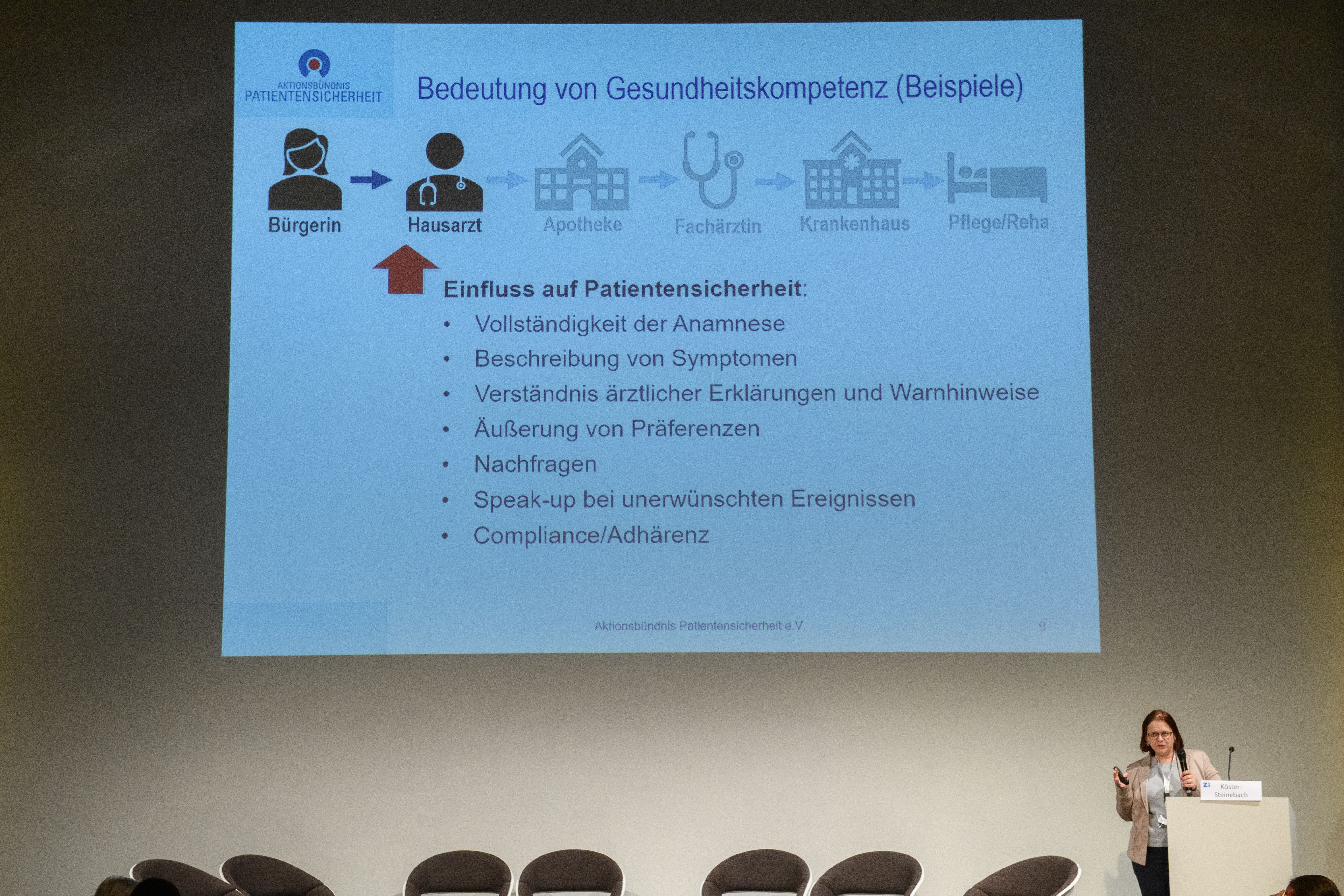 Während des Vortrags einer Frau wird ihre Powerpoint-Präsentation hinter ihr an die Wand projiziert.